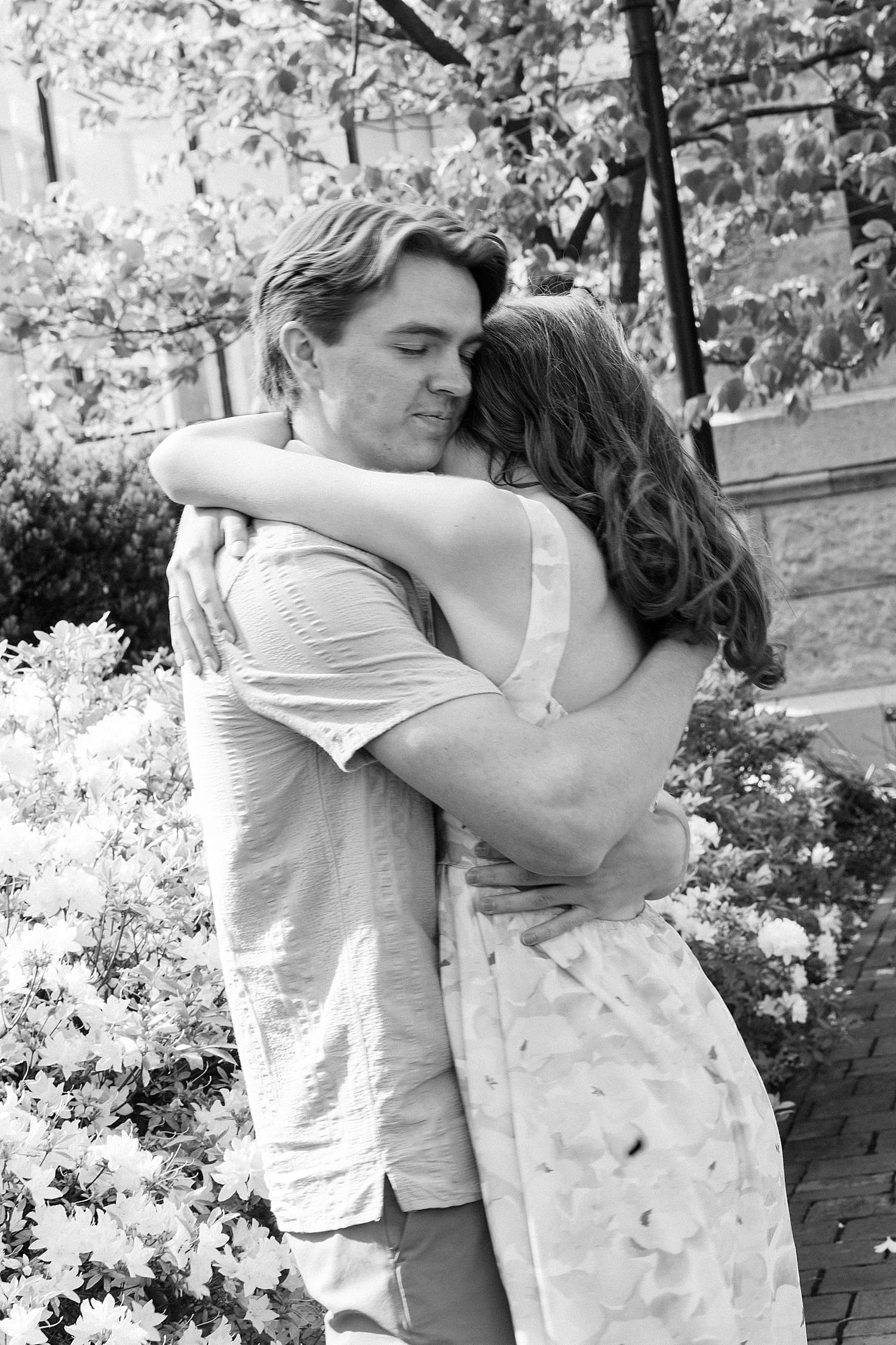 couple embraces tightly in front of cherry blossom tree by St. Louis wedding Photographer