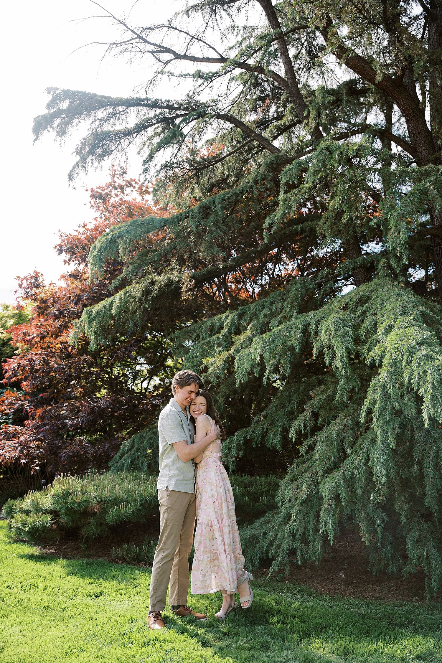 man hugs woman closely under large tree by St. Louis wedding Photographer