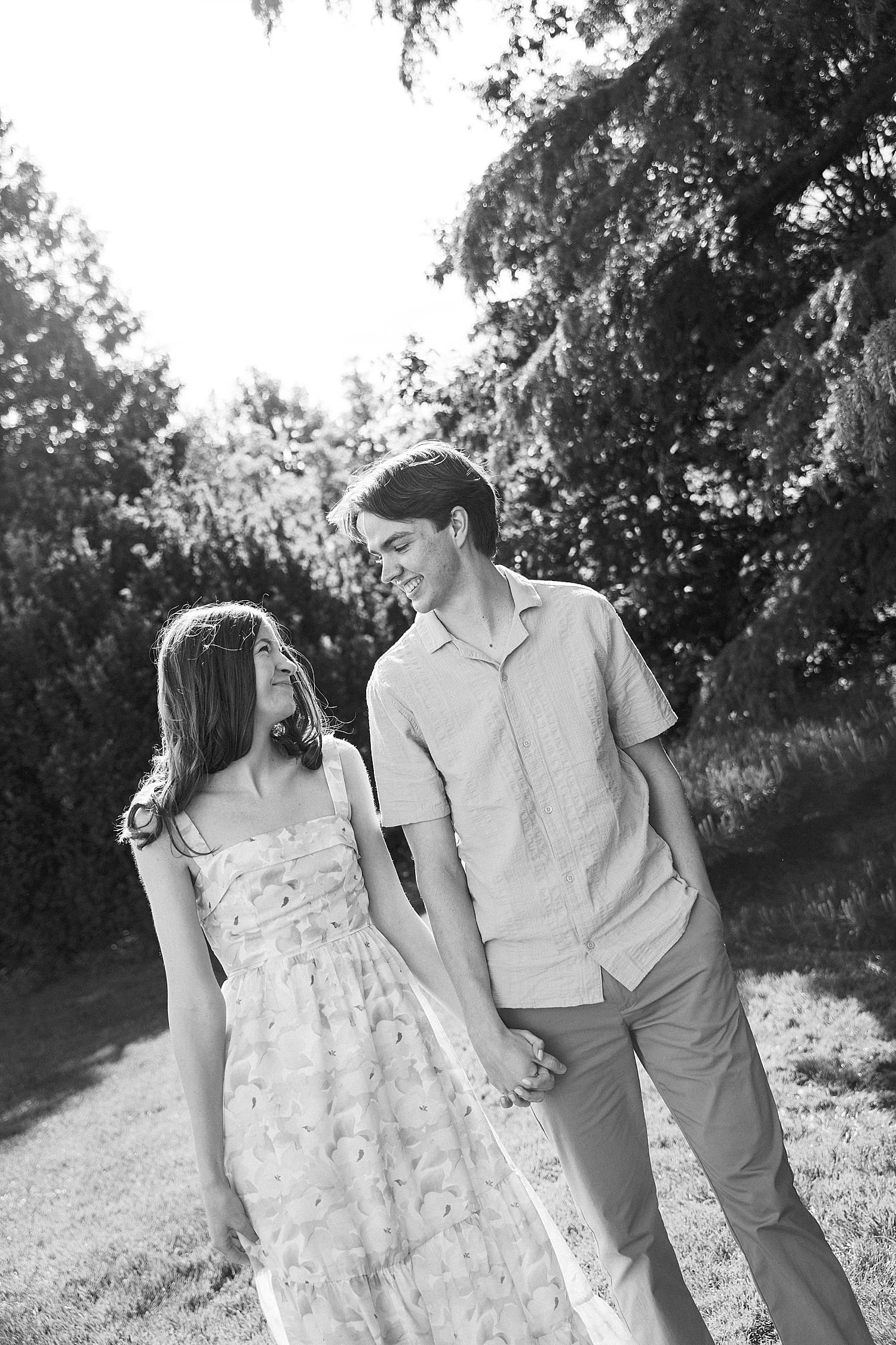 engaged couple walk hand in hand through trees for wandering session