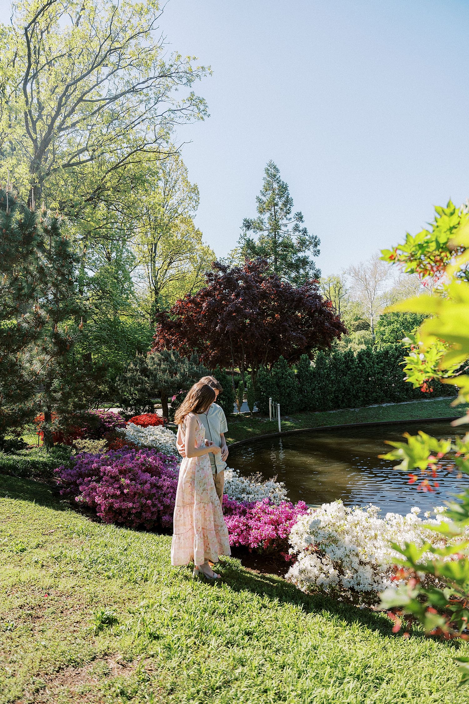 engaged couple stand next to flowers near pond by St. Louis wedding Photographer