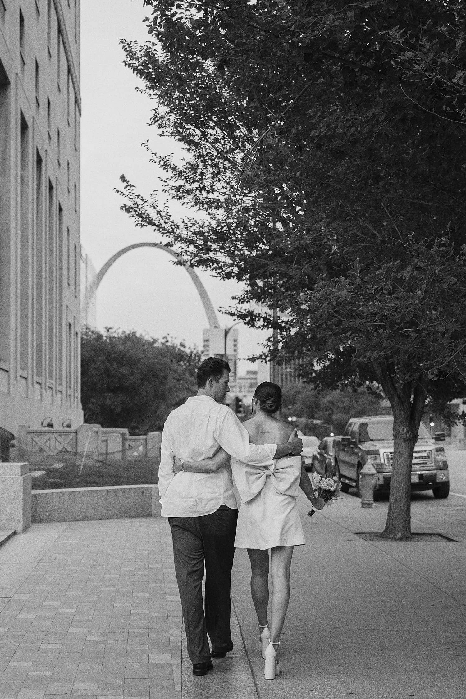 couple walks down the street in front of Arch for editorial elopement session