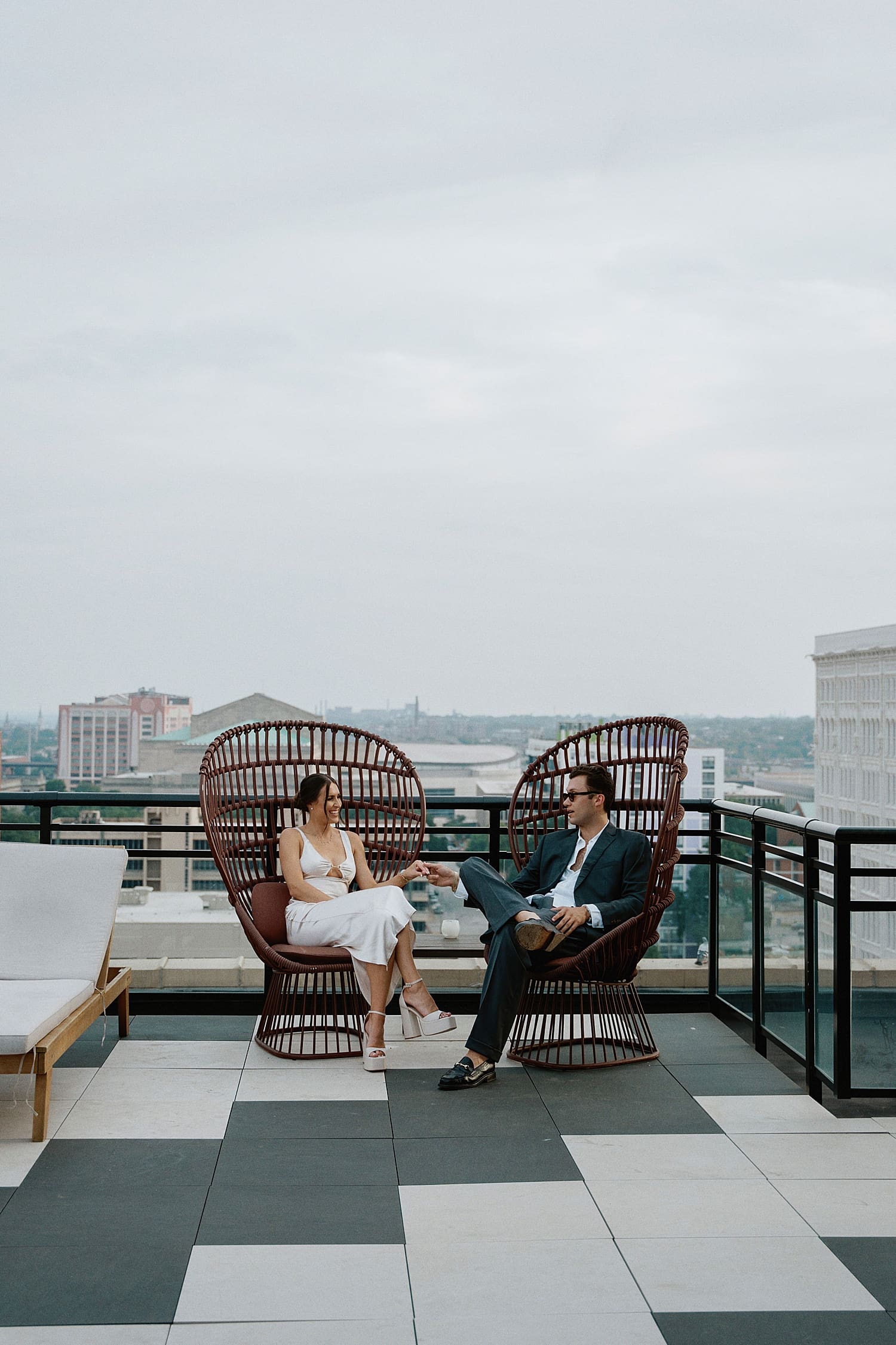 newlyweds sit in large outdoor chairs on rooftop by St. Louis Wedding Photographer