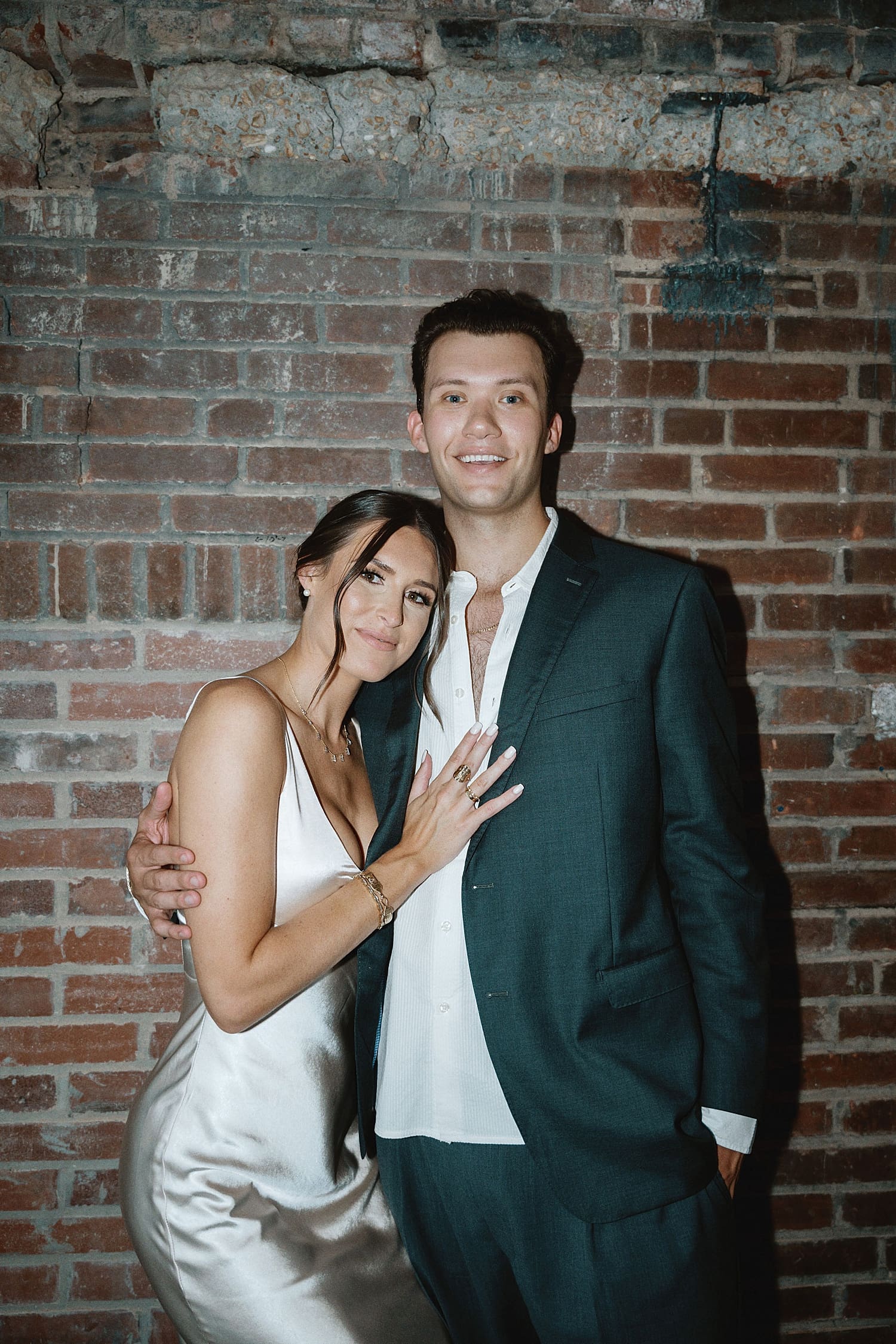 newlyweds snuggle together in front of a brick wall by Camille Meers Photography