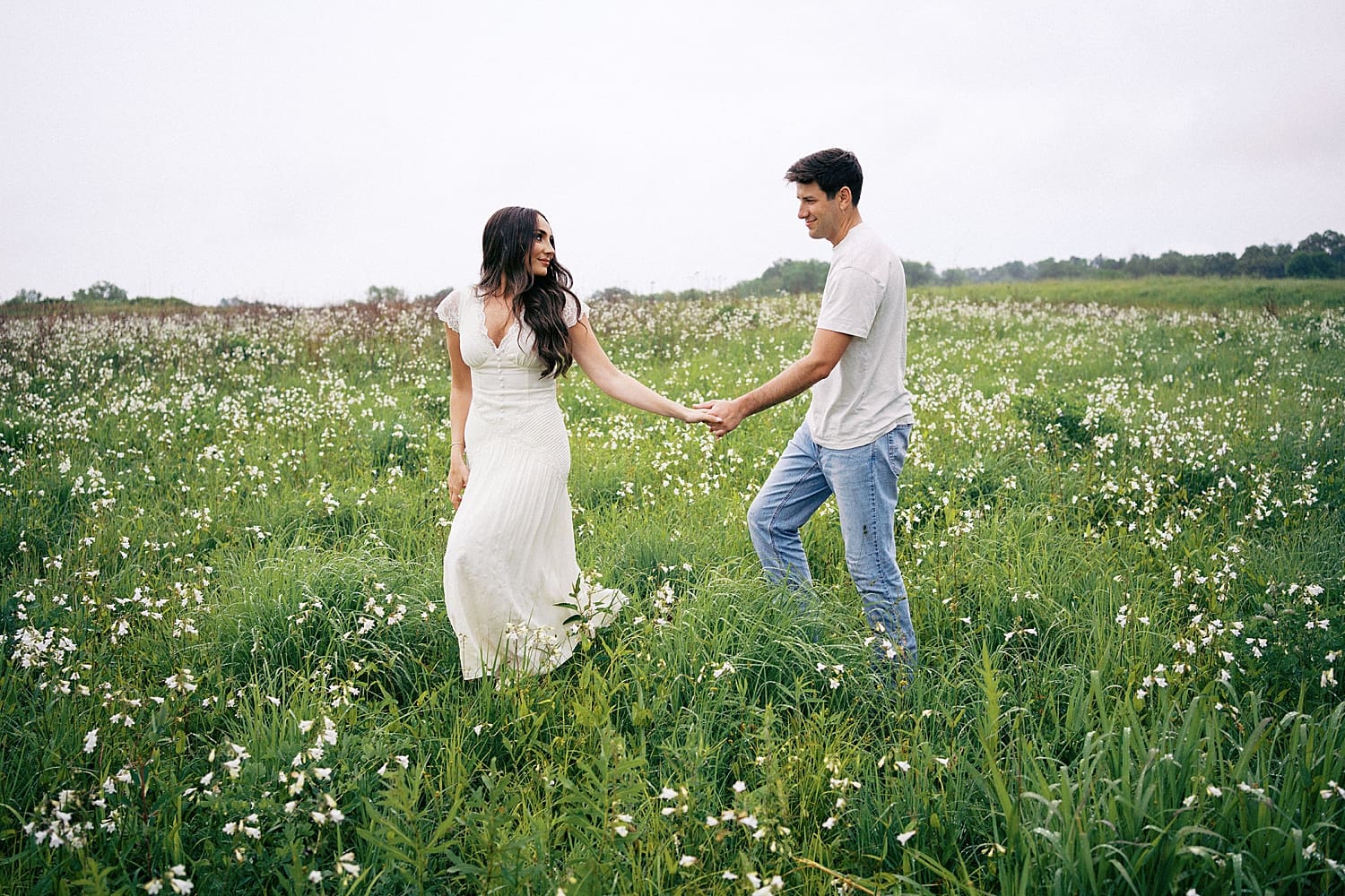 engaged couple hold hands as they walk through green field by Camille Meers Photography
