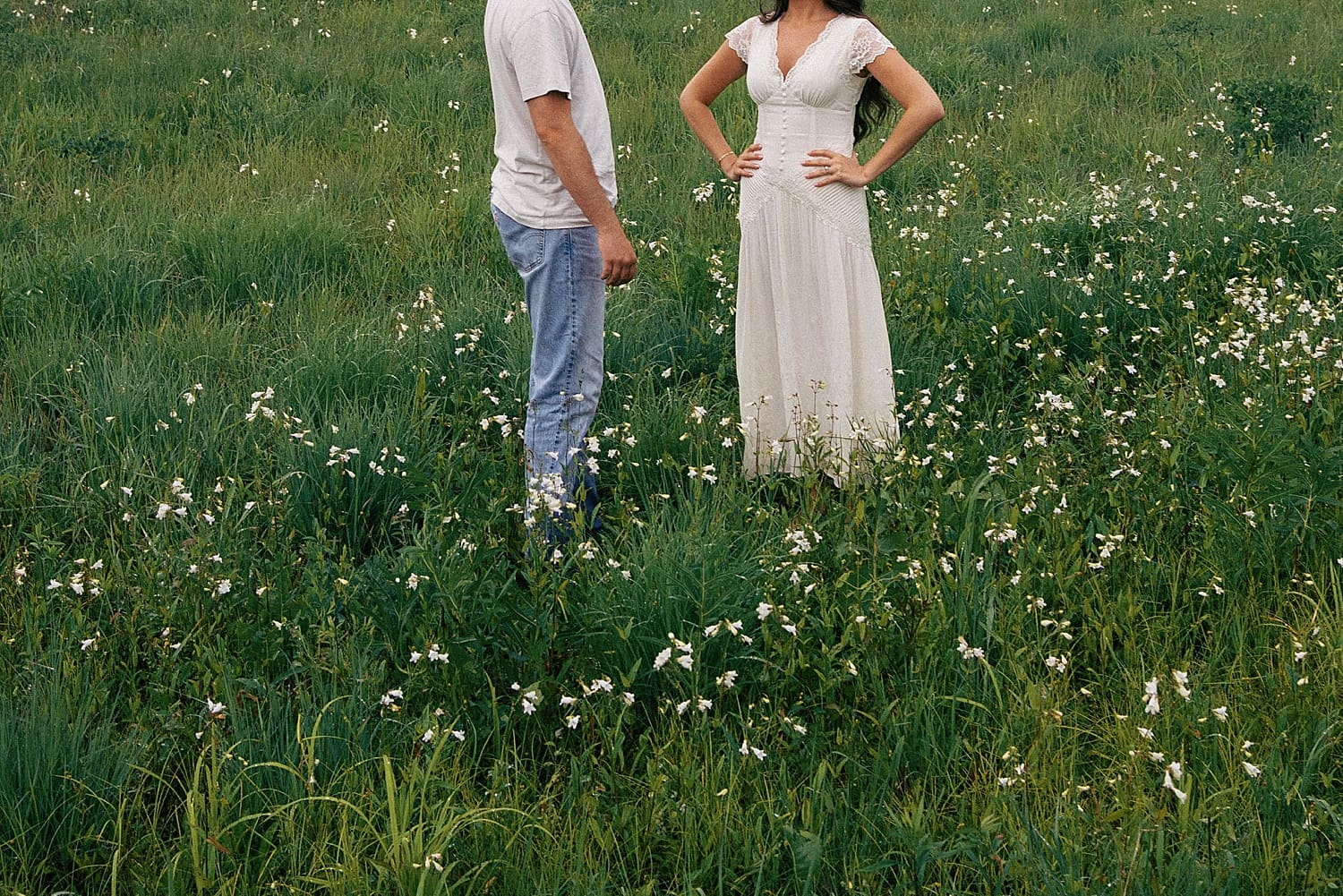 two people stand in rich green grass dotted with white flowers by Camille Meers Photography