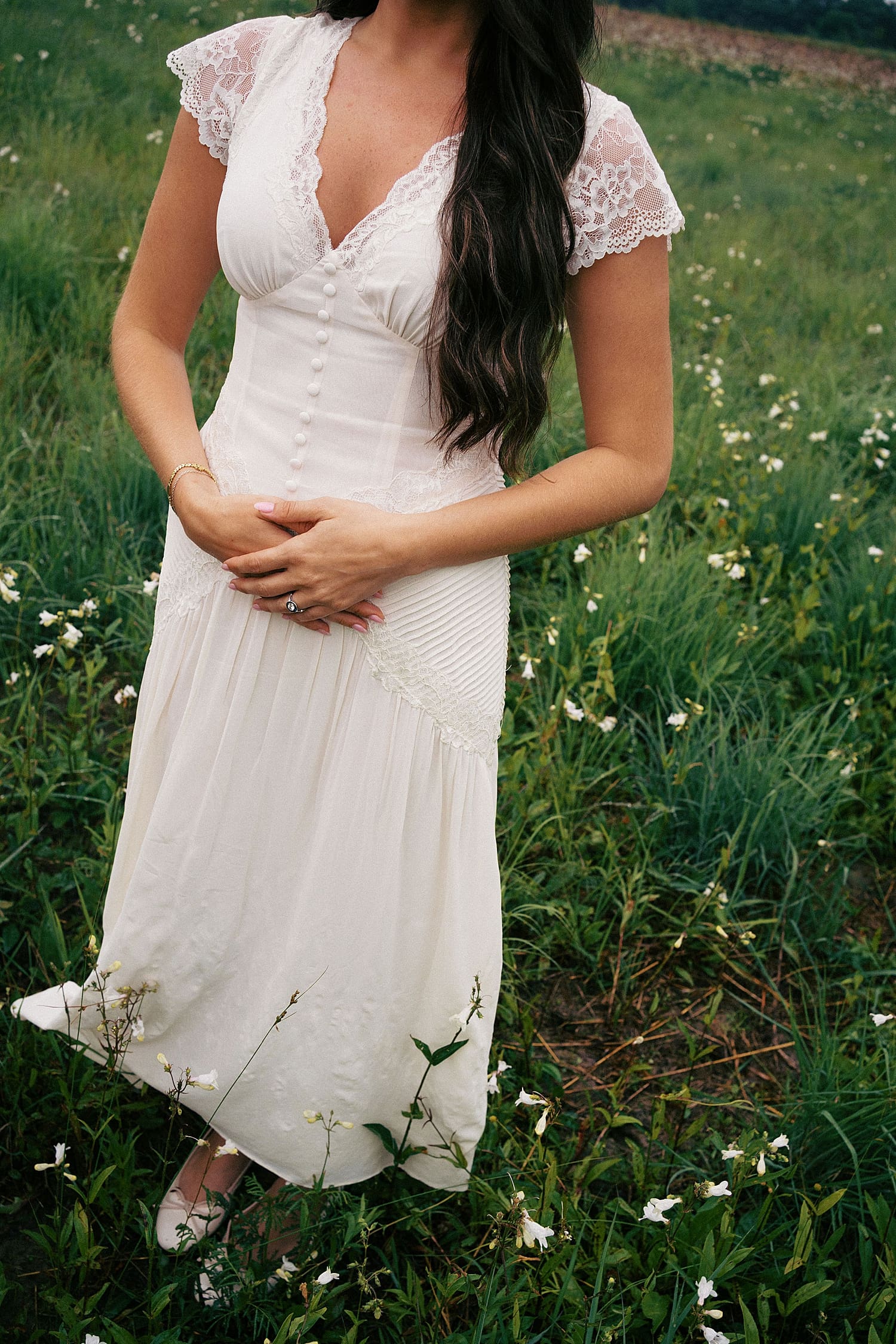 woman in white lace dress stands in wildflowers by St. Louis wedding photographer