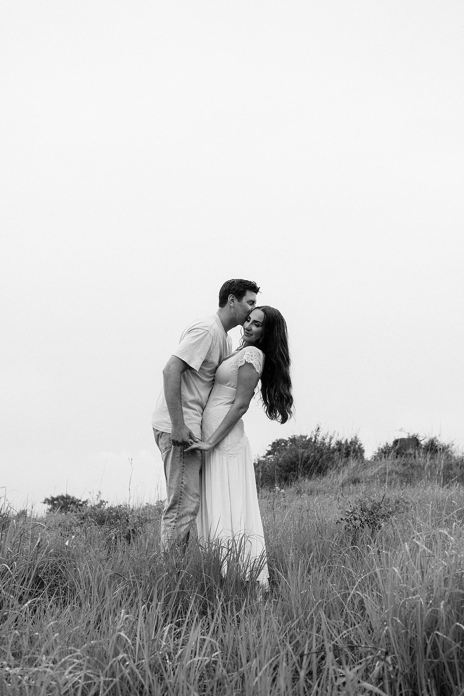 A fiance leans in to kiss his girl in field by St. Louis wedding photographer