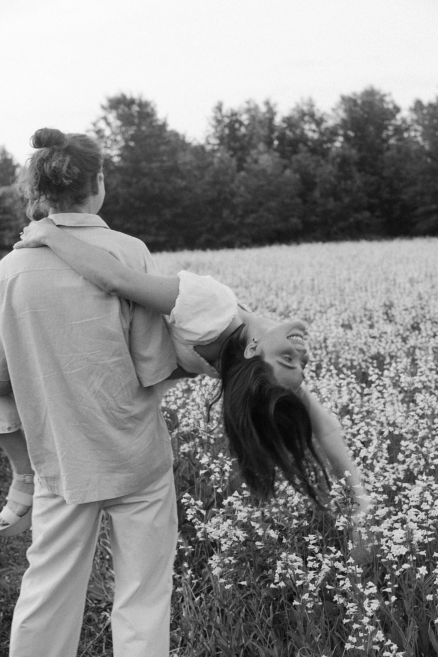 man carries his woman through flowers for best time for Spring engagement photos