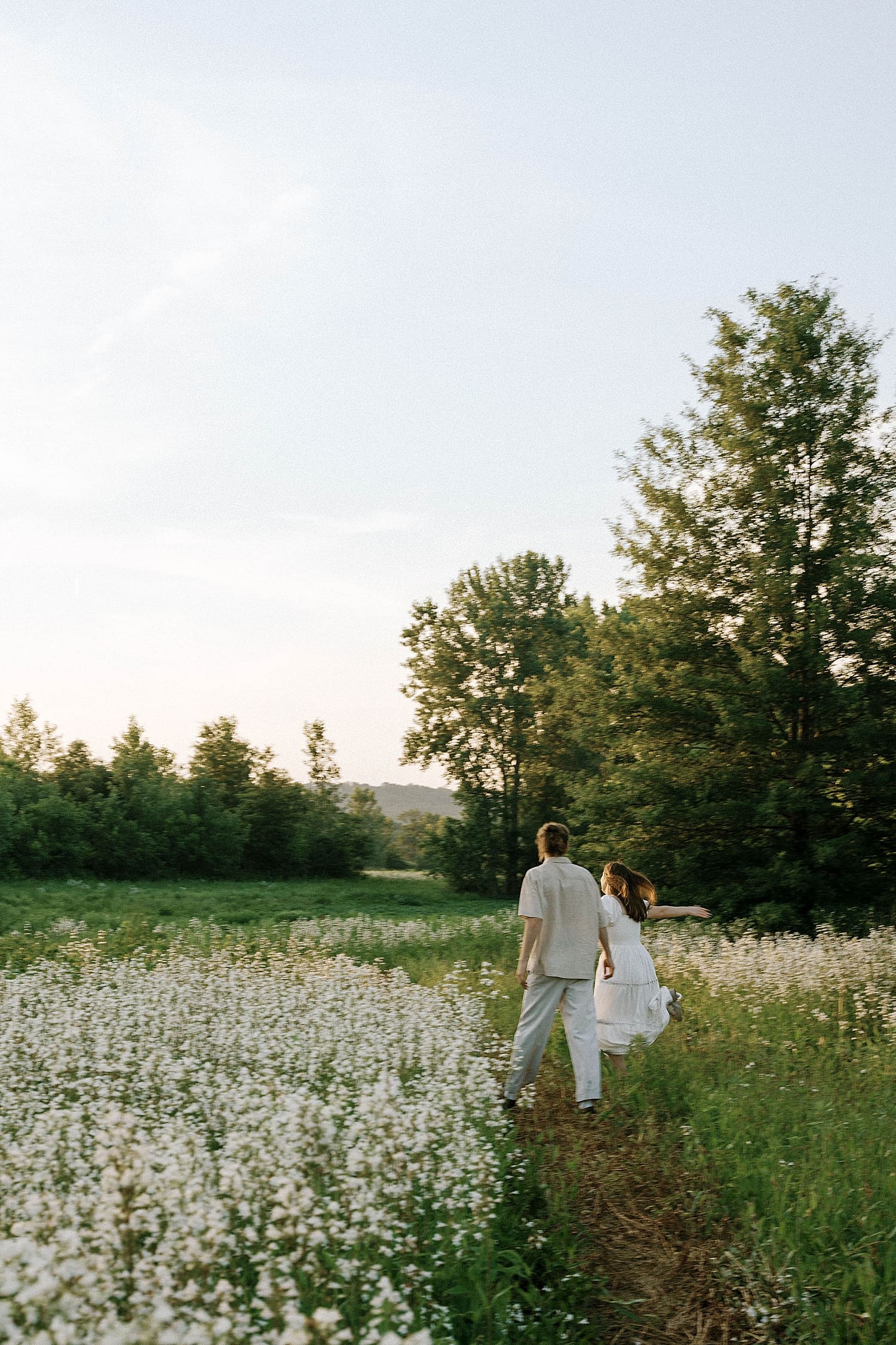 man and woman laugh and run together through flowers by Camille Meers Photography