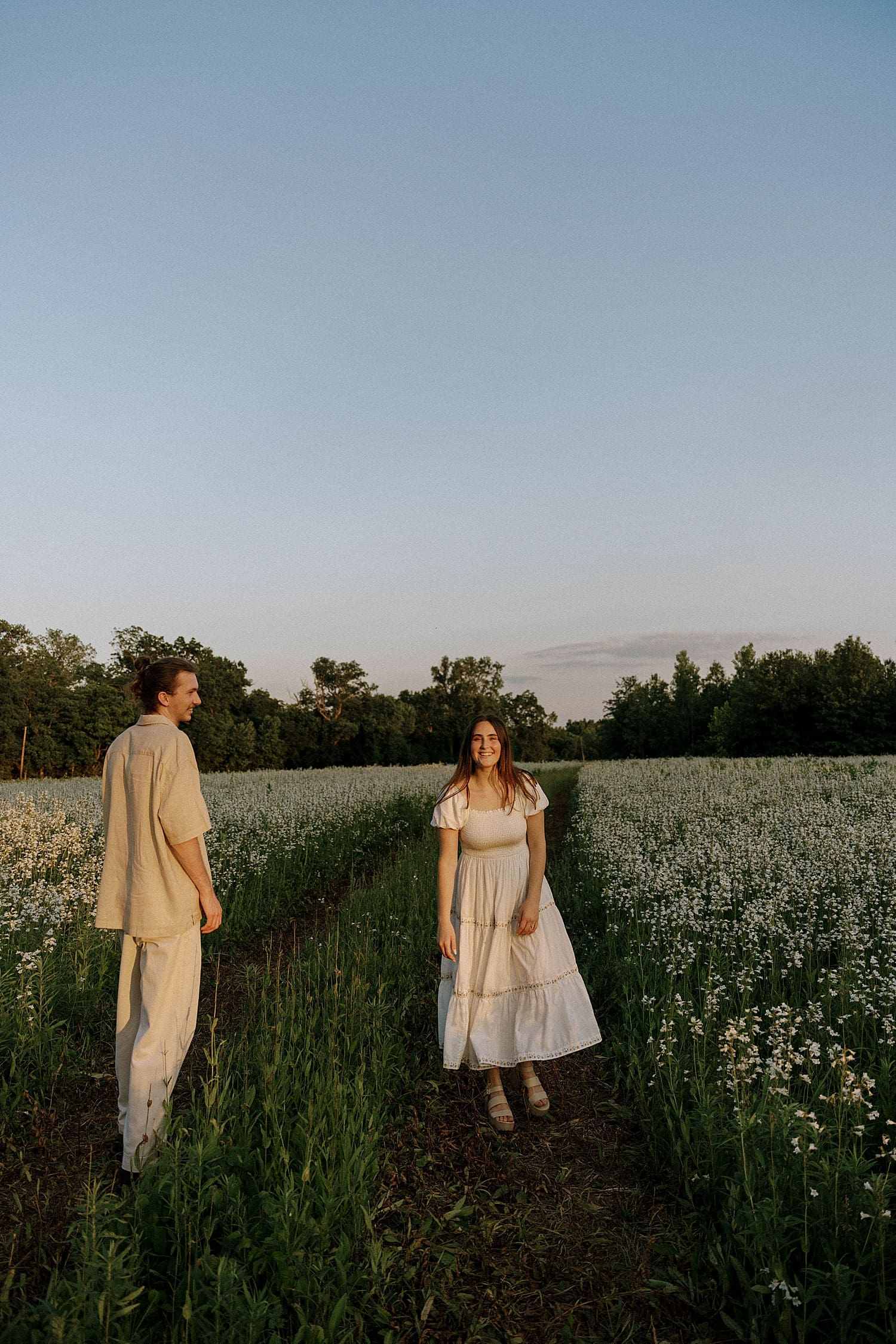 couple stands together in white flower field for best time for Spring engagement photos