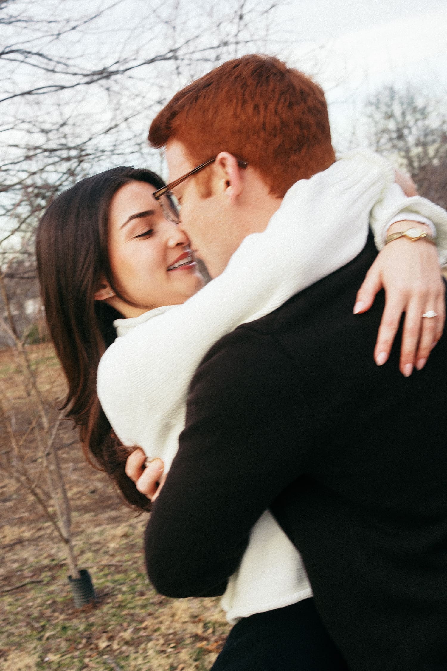 couple embraces in front of winter trees showing your engagement session should happen where you live