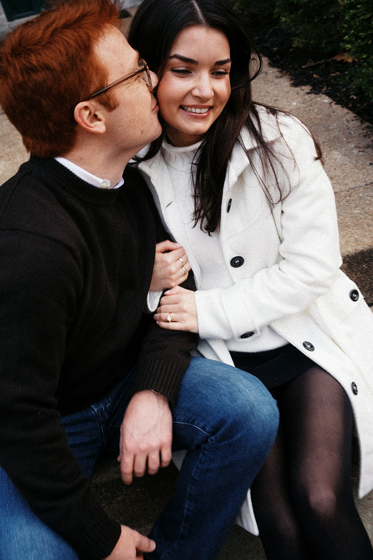man kisses woman while they sit on sidewalk curb showing your engagement session should happen where you live