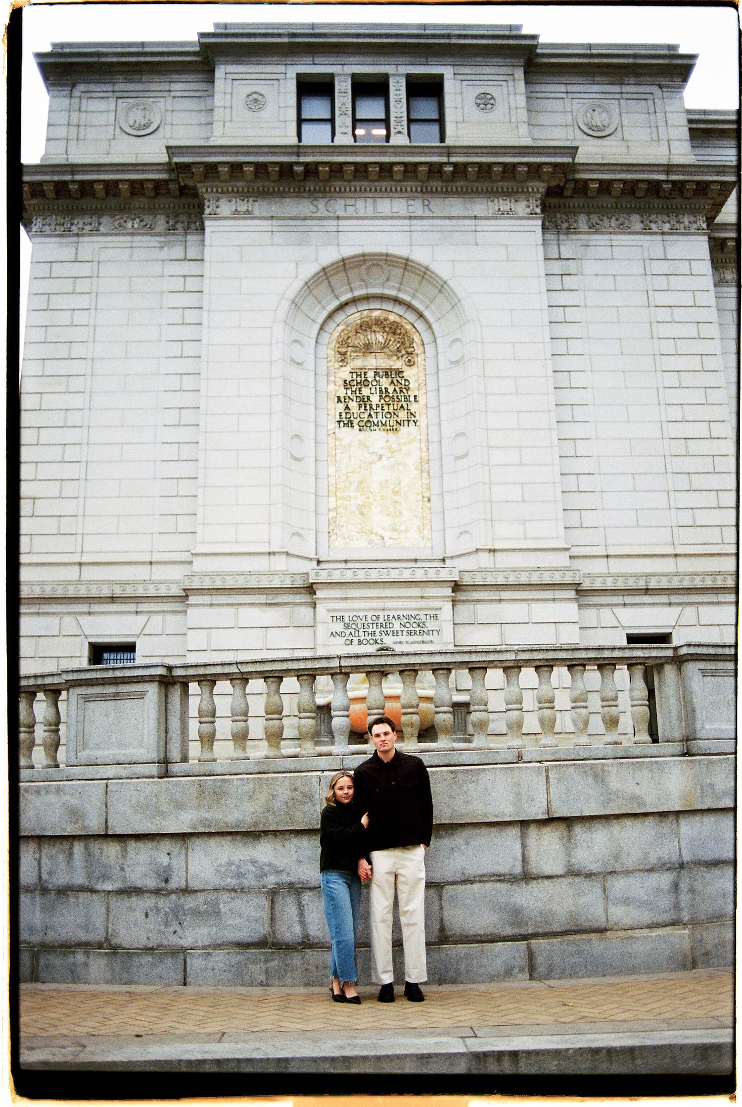 engaged couple stand in front of large city building by Camille Meers Photography