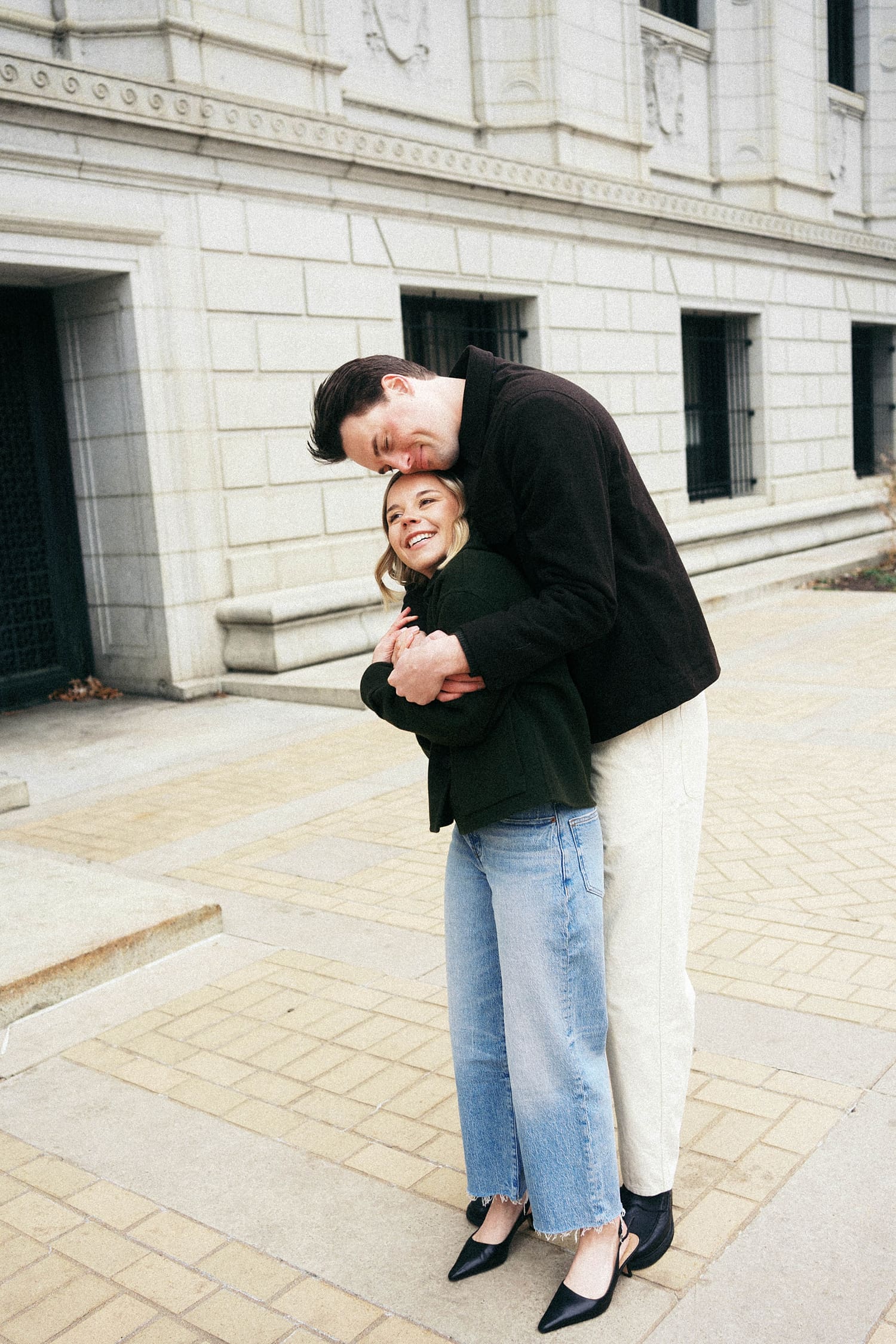 man leans over his petite fiance after learning how to feel natural in engagement photos