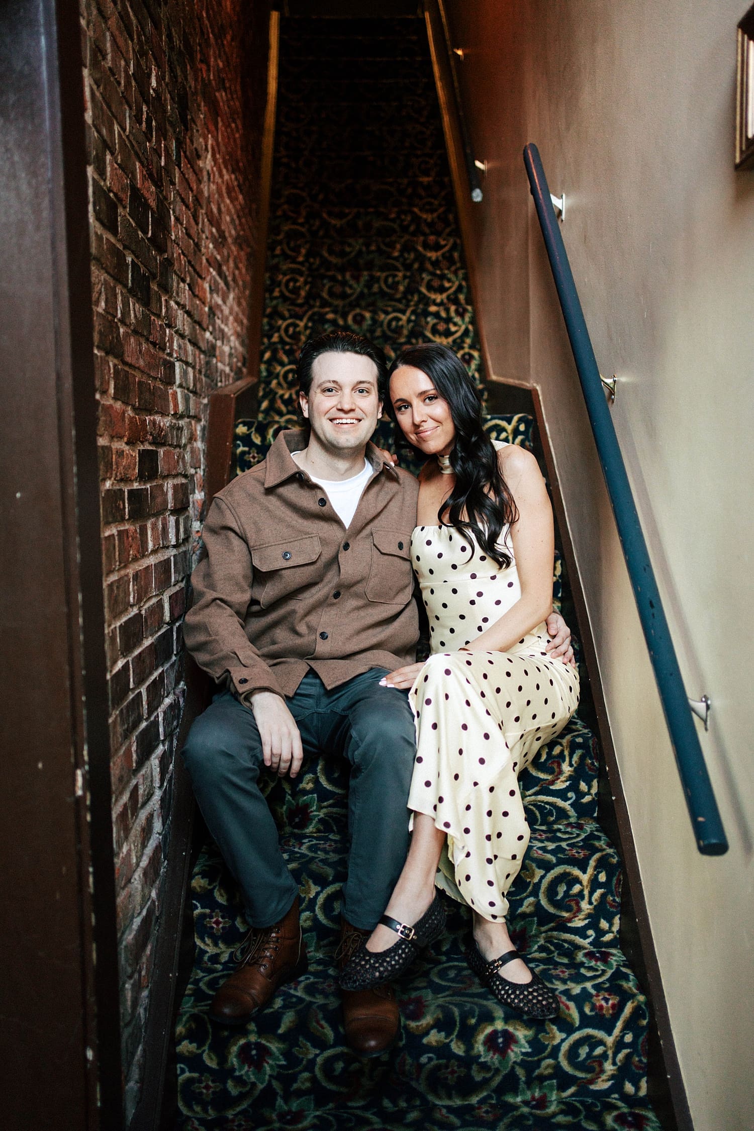 two people sit on carpeted staircase in restaurant by St. Louis wedding photographer