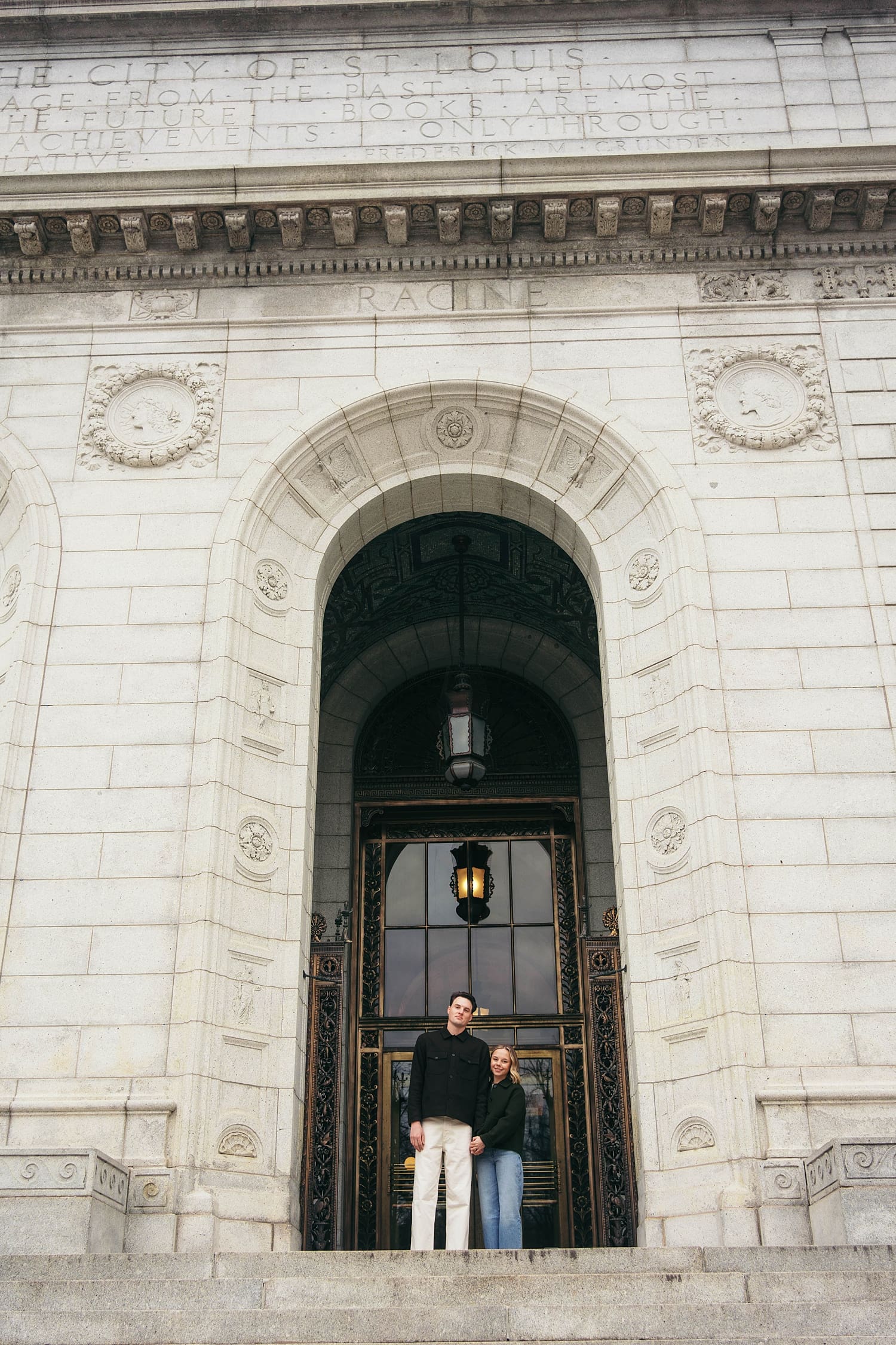 engaged couple stand in very large ornate stone doorway by Camille Meers Photography