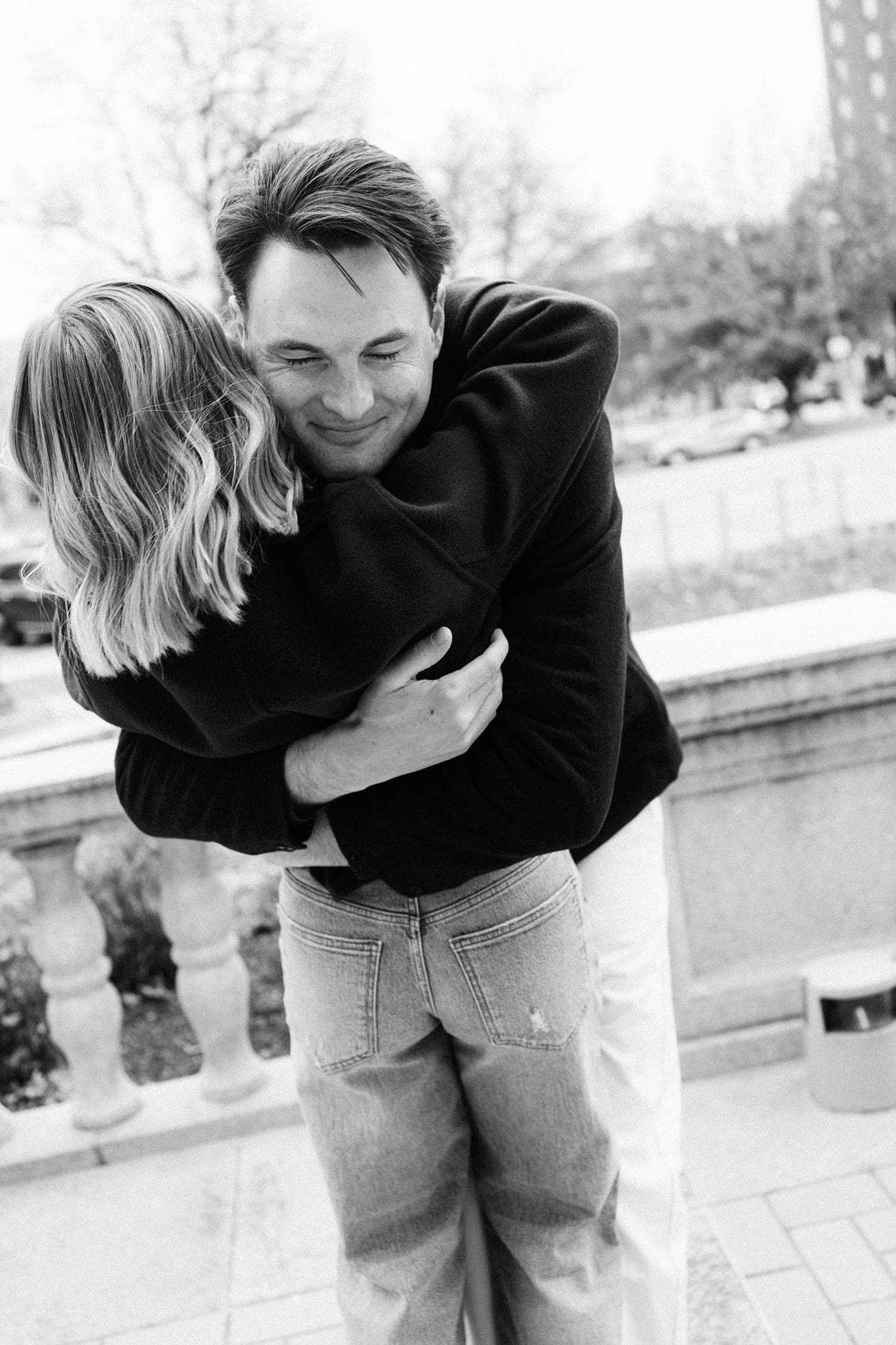 groom-to-be holds his woman close on the sidewalk after learning how to feel natural in engagement photos