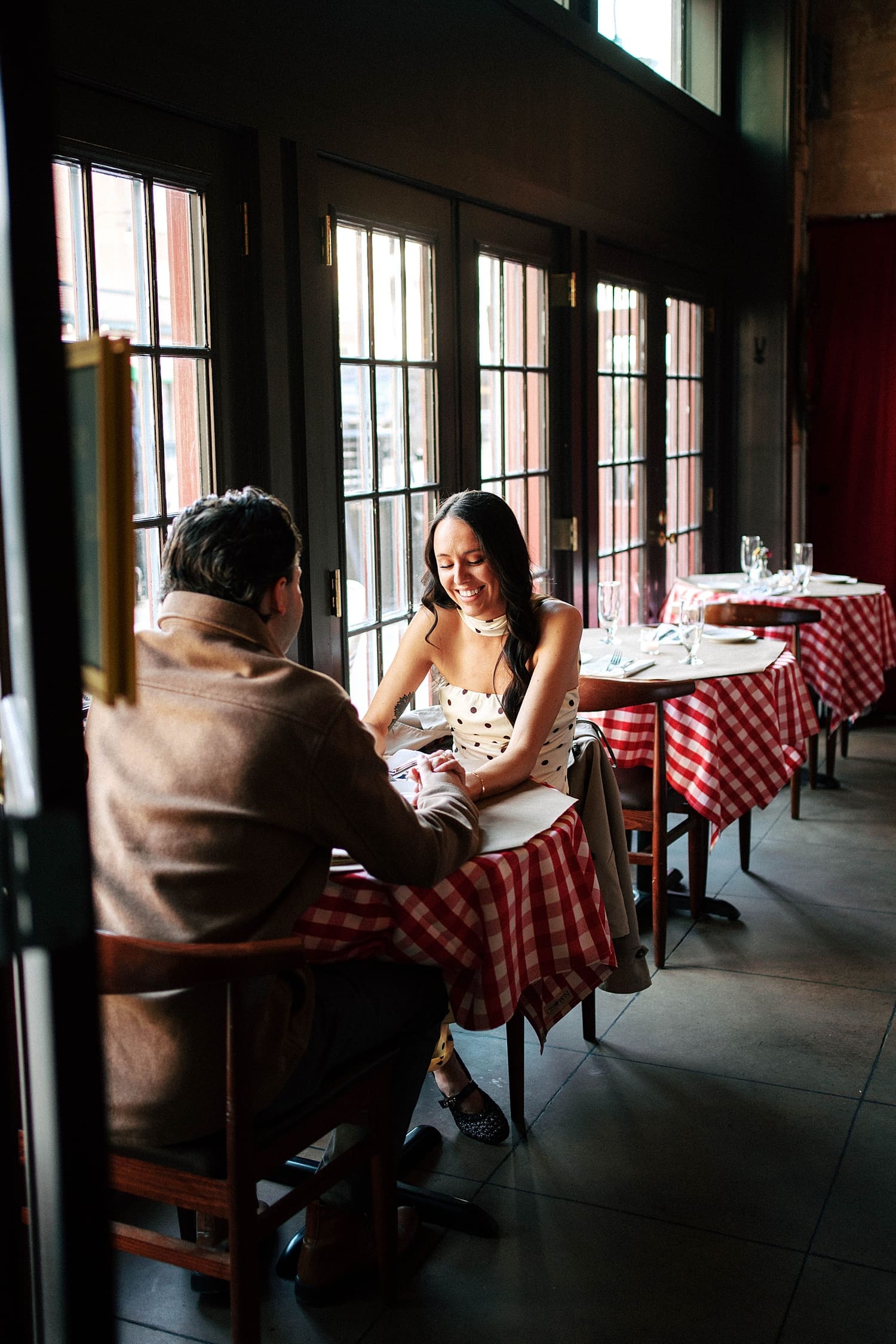 brunette woman in polka dot dress sits across from fiance at restaurant by Camille Meers Photography