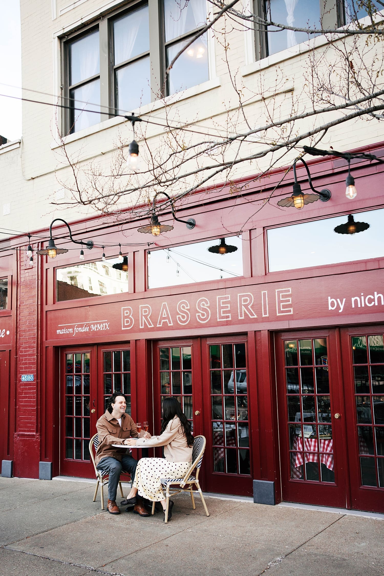 couple sits at table outside of red restaurant by St. Louis wedding photographer