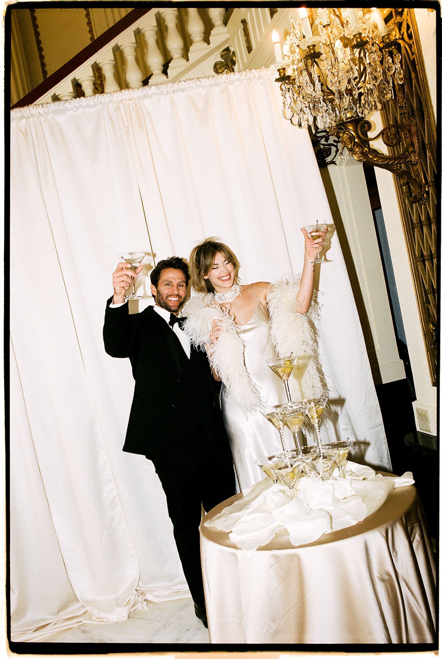 husband and wife raise a cheers in front of white curtain by St. Louis wedding photographer