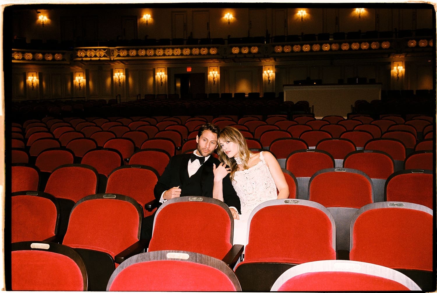 man and woman sit in red auditorium chairs in Powell Hall