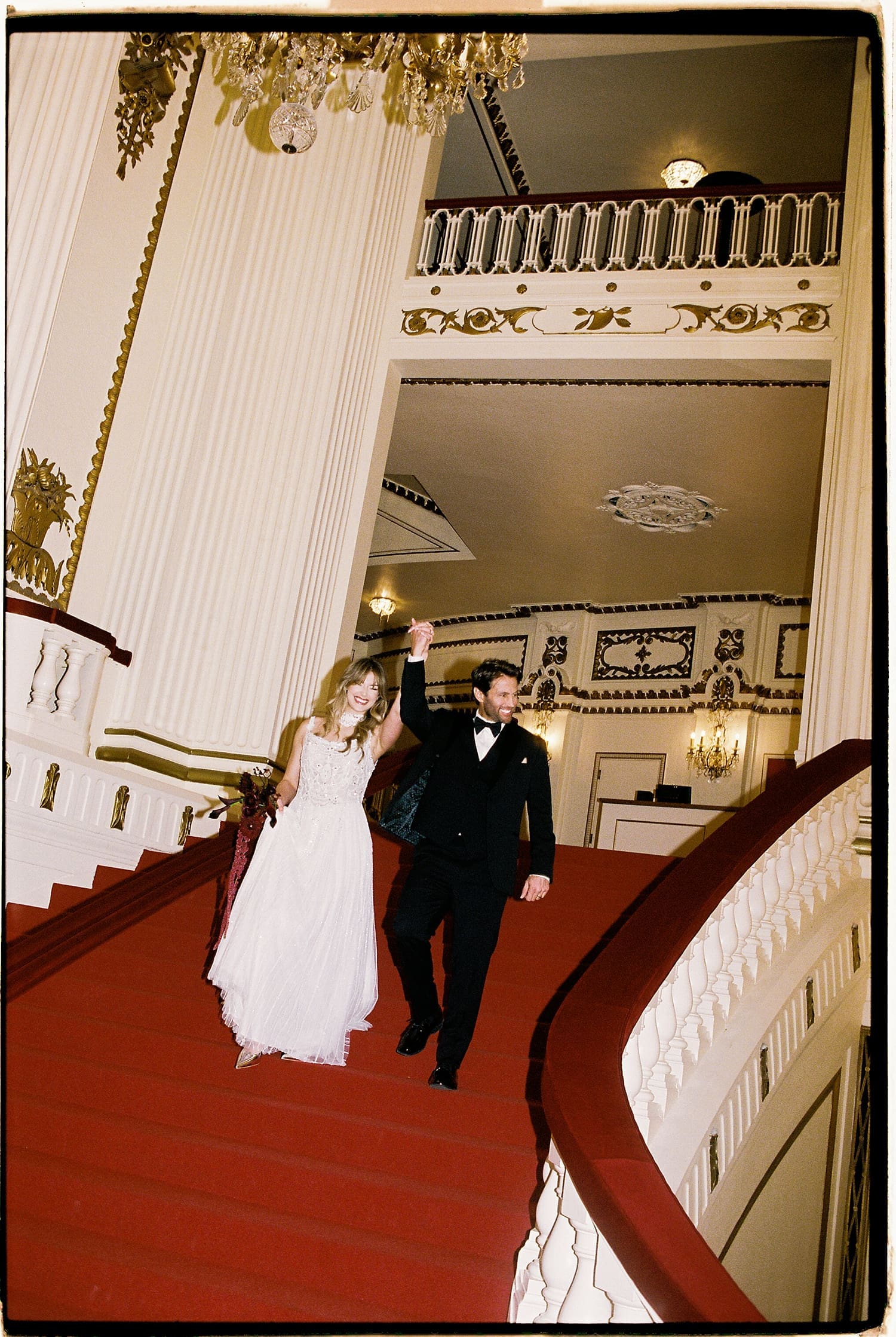 newlyweds walk down big red staircase at Powell Hall
