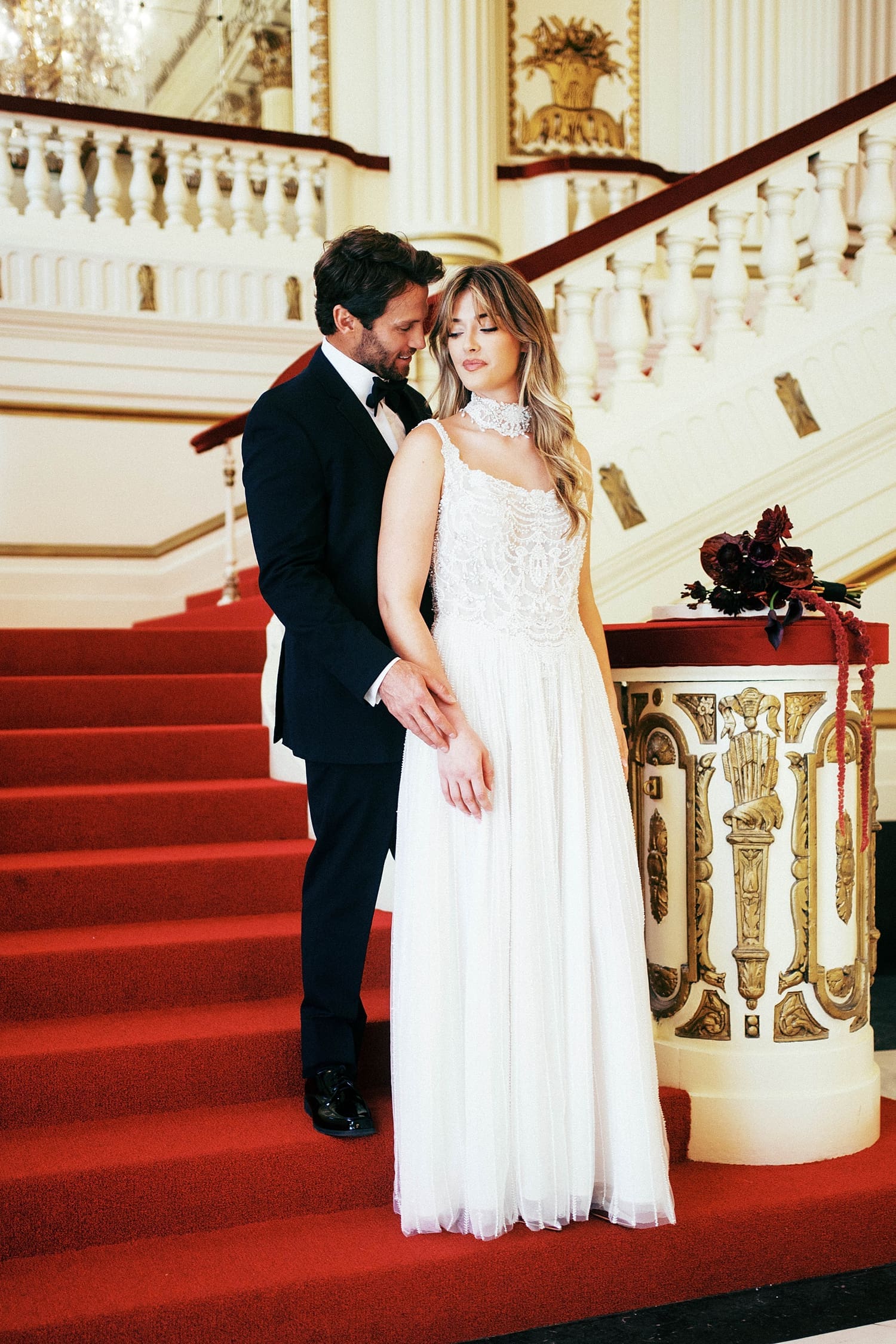 man holds his bride close on red carpeted stairs by Camille Meers Photography