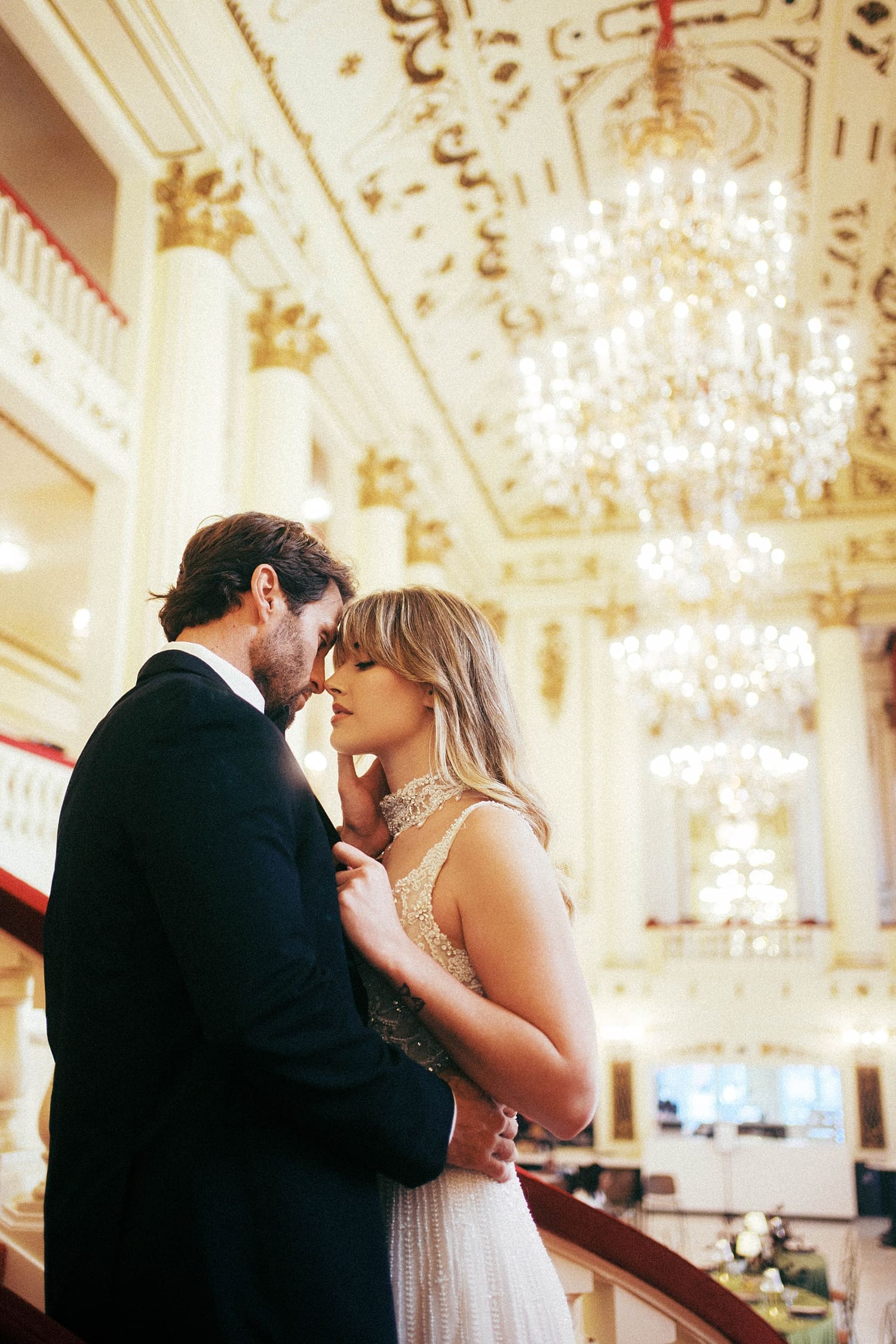 newlyweds stand under row of chandeliers on the ceiling by St. Louis wedding photographer