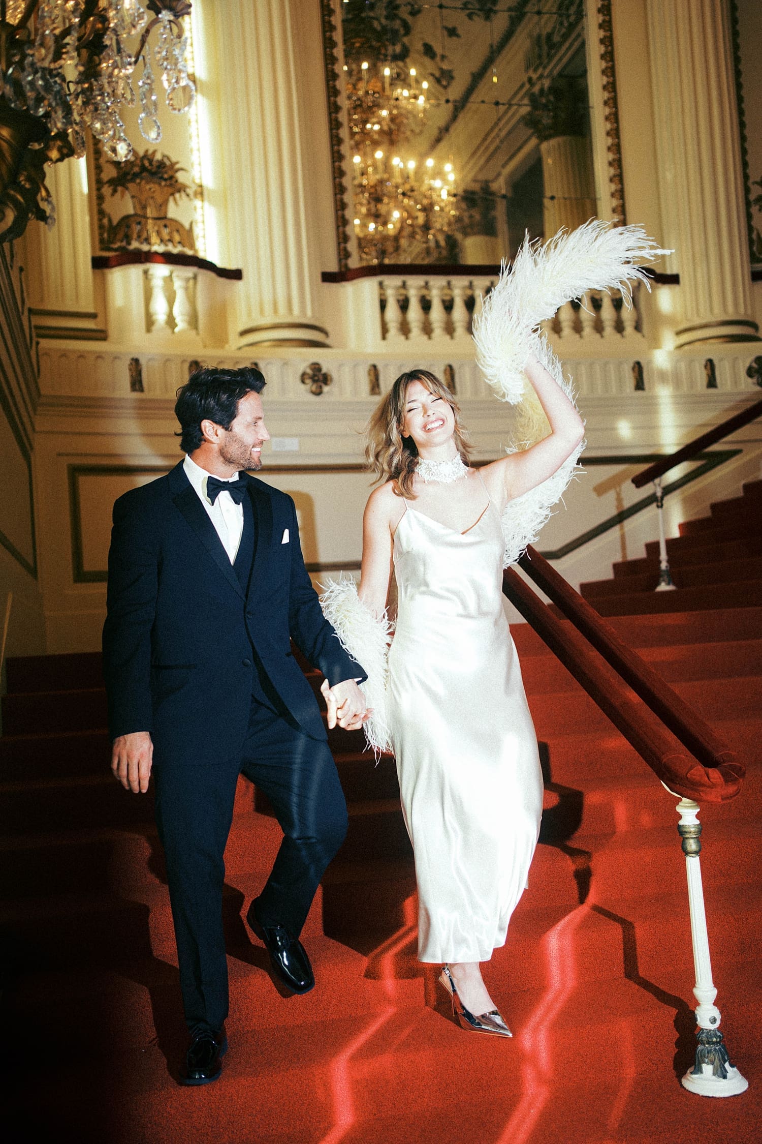 bride and groom walk down big red staircase at Powell Hall