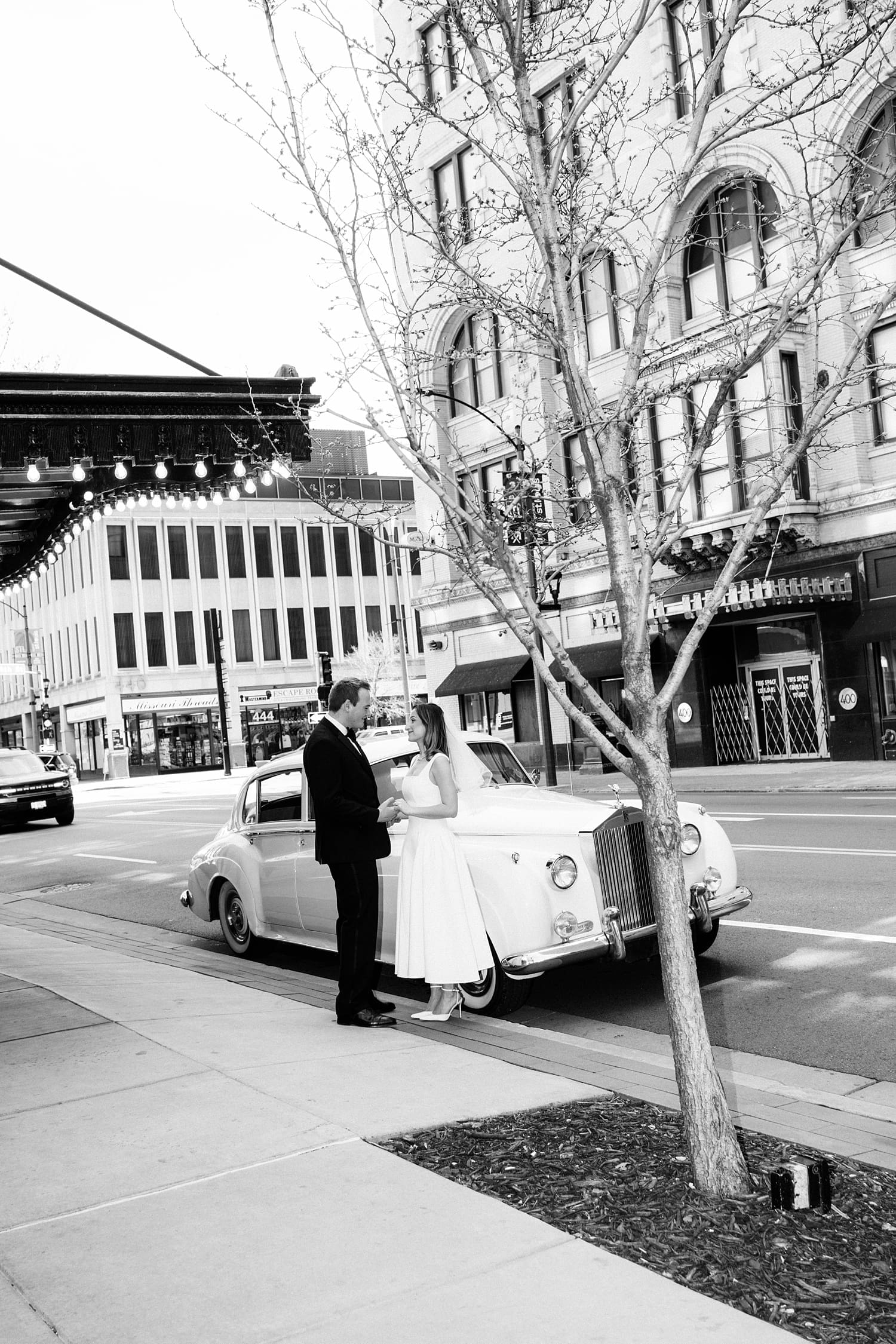 husband and wife stand in front of rolls royce on sidewalk at the Missouri Athletic Club