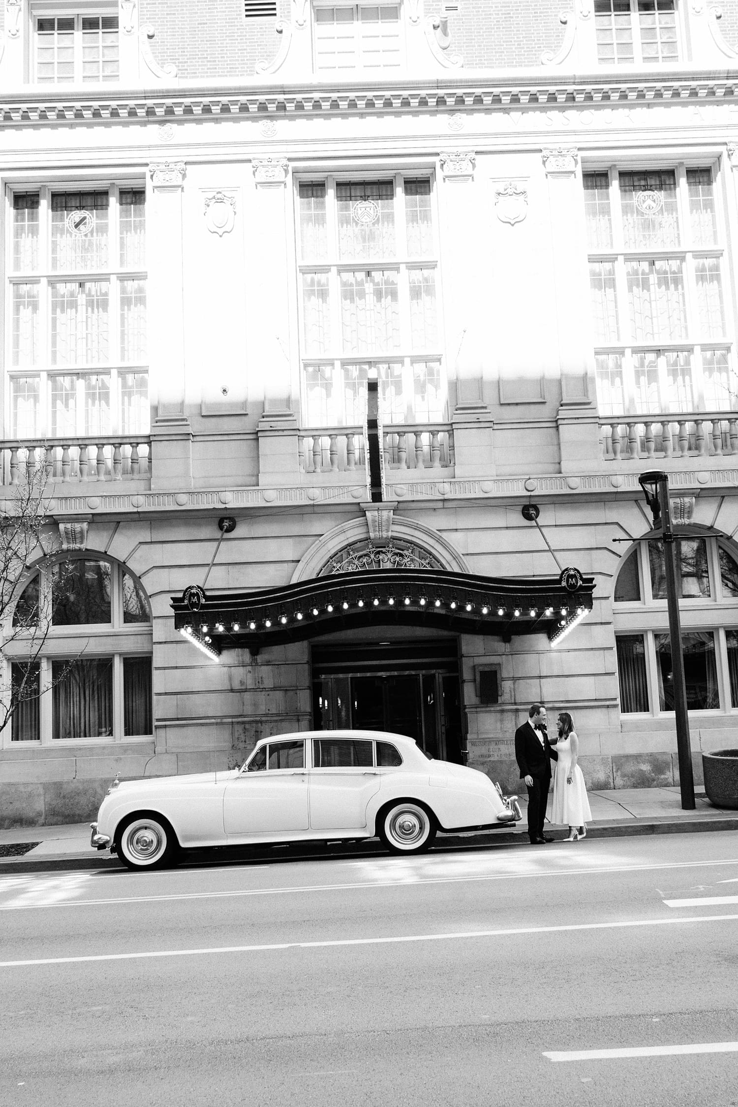 couple stand on the street next to old car by Camille Meers Photography