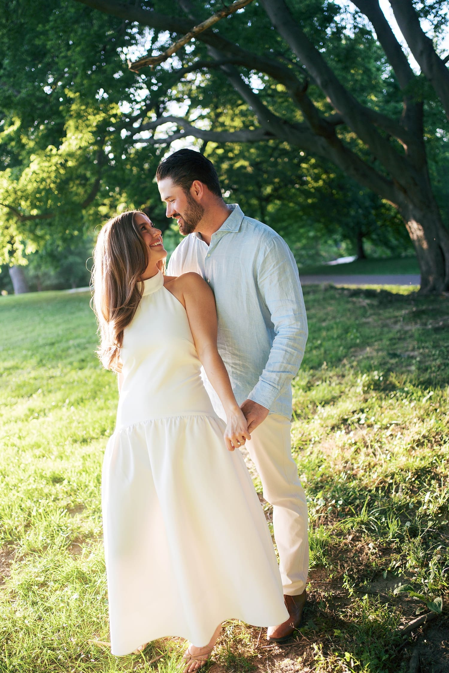 man holds his fiancé's hand under big trees for unposed engagement session