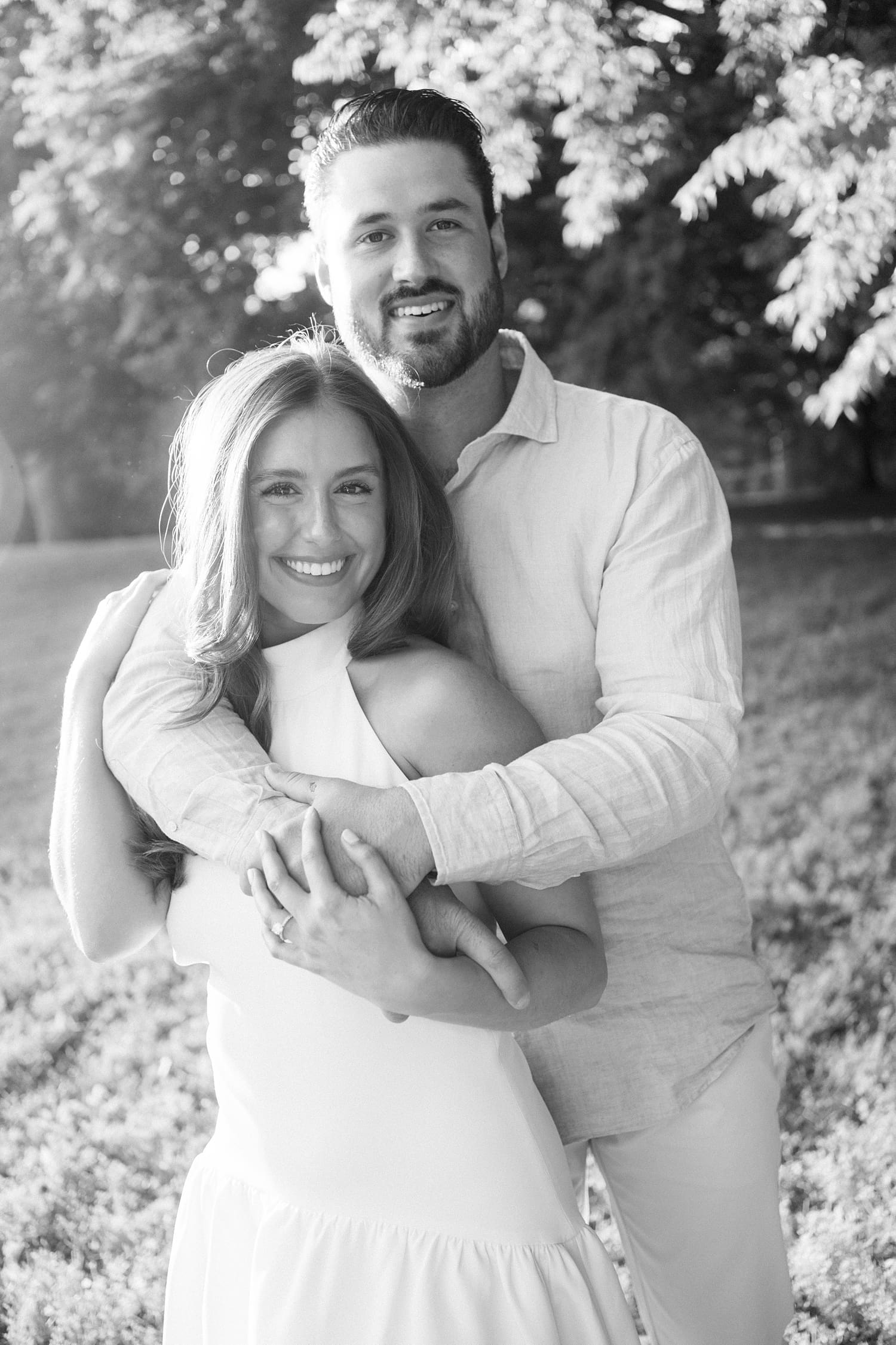 couple stands together in front of large trees by documentary wedding photographer