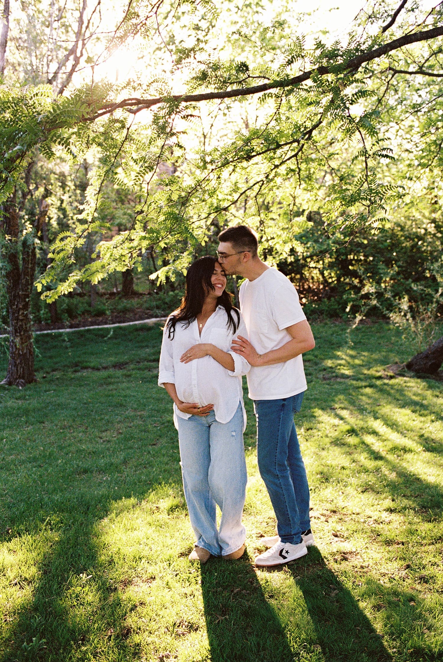 couple embrace under backyard tree for candid maternity photo session