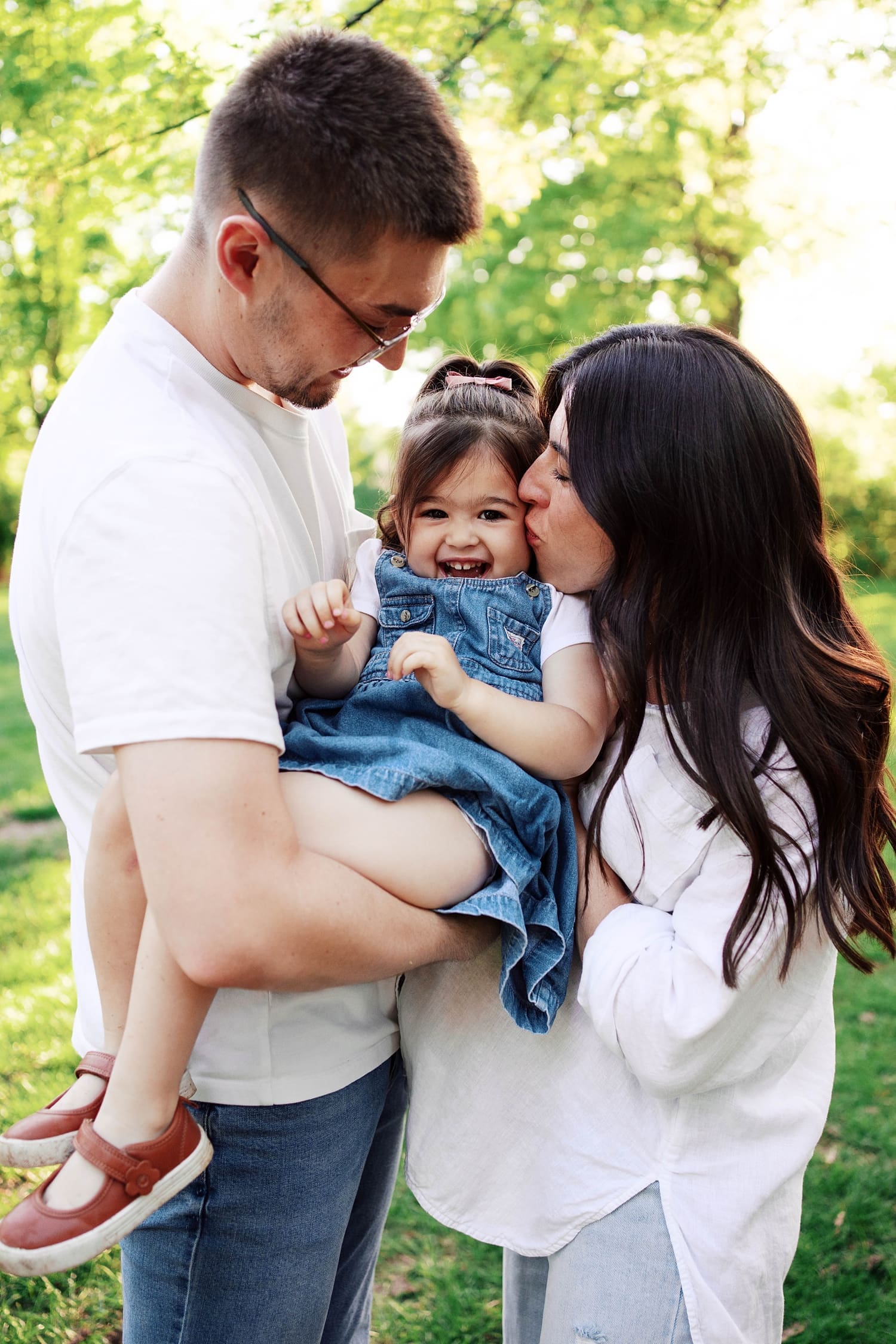 mom kisses her little kid while dad holds her by Camille Meers Photography