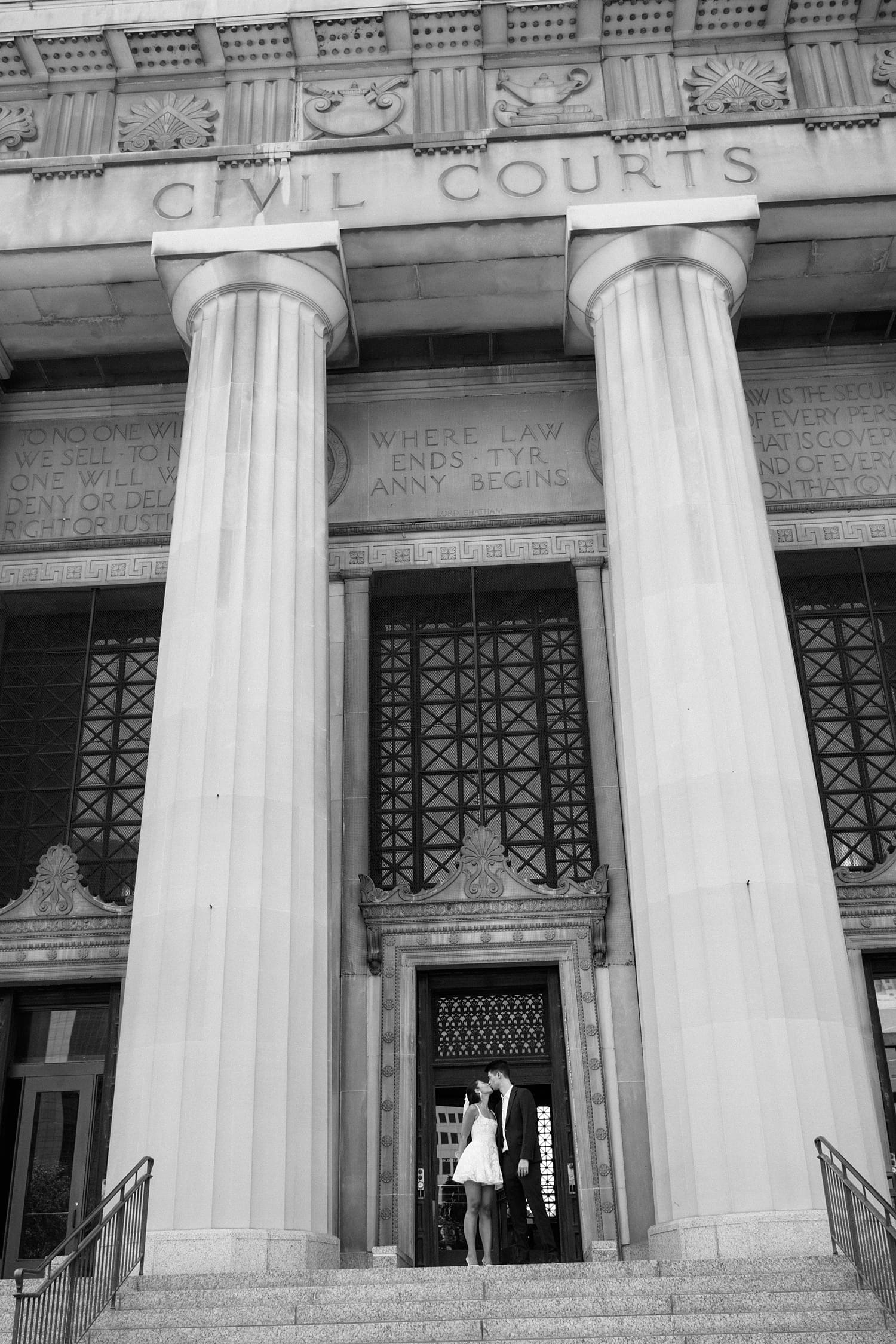 couple stand under large columns at government building after eloping by Camille Meers Photography