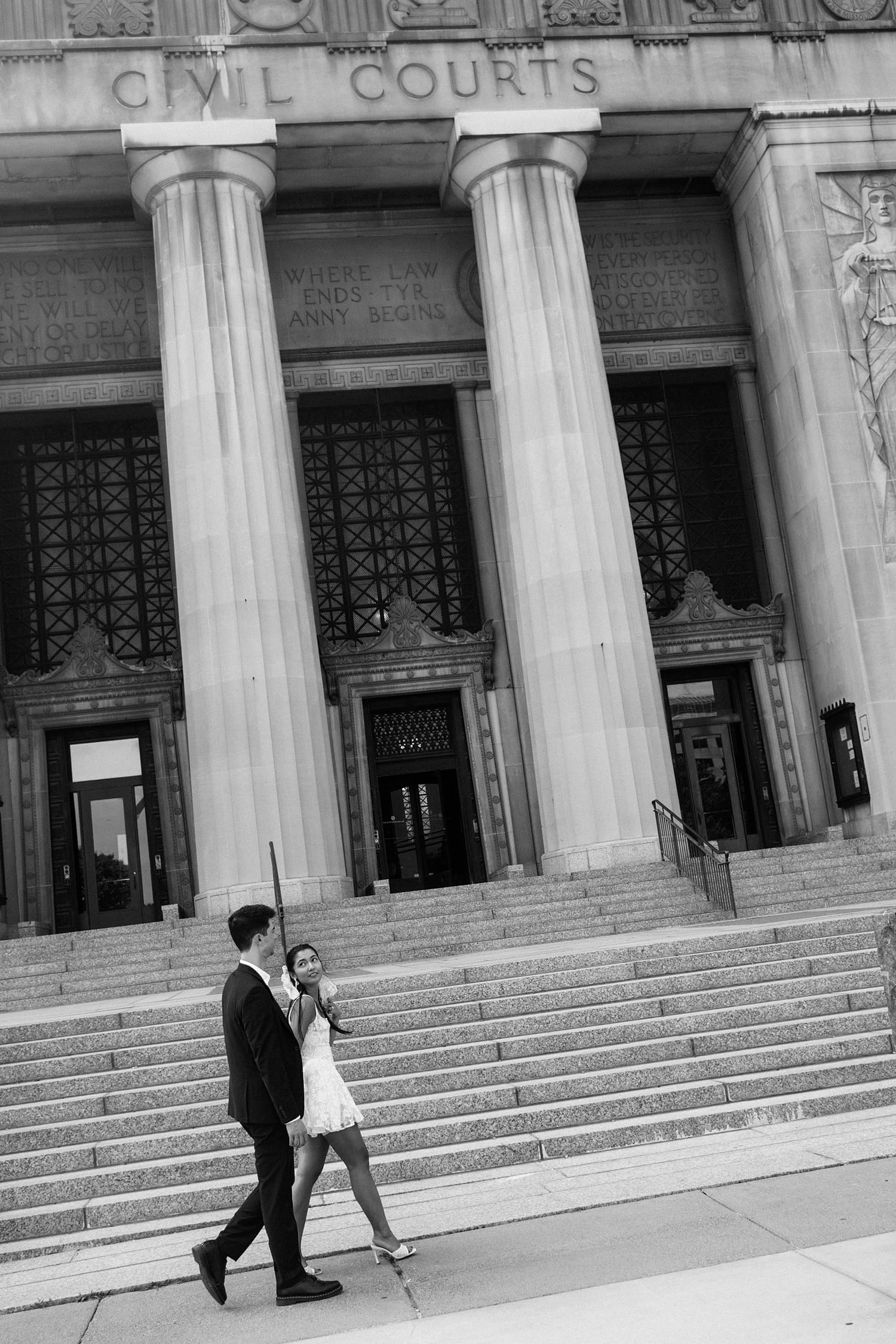 Newlyweds walk down the sidewalk in front of historic building by Camille Meers Photography