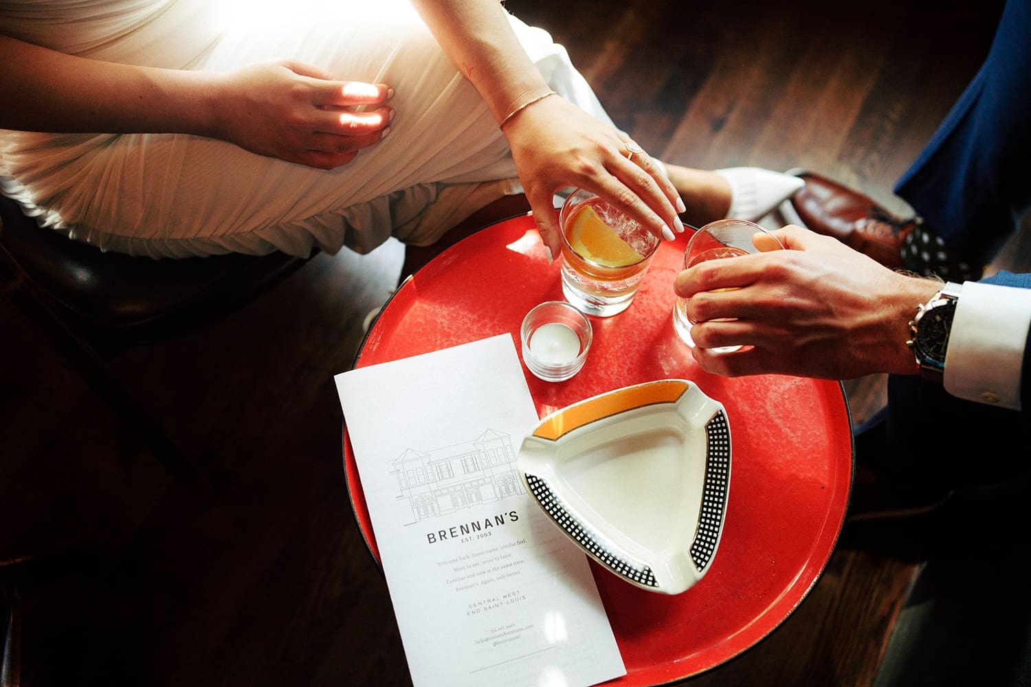 two hands touch cocktails on little red table by Camille Meers Photography