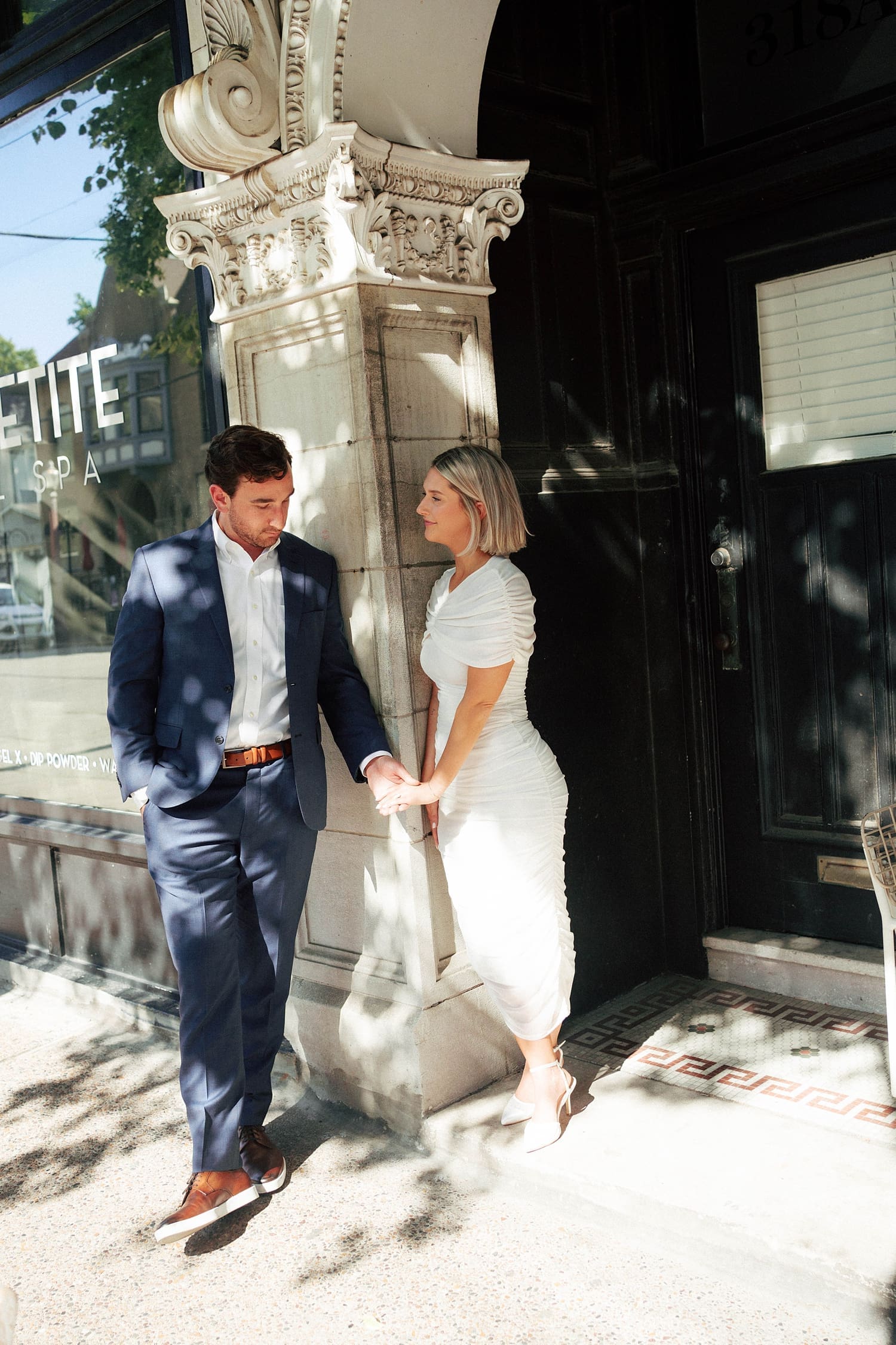 man leans on pillar and holds fiance's hand by Camille Meers Photography